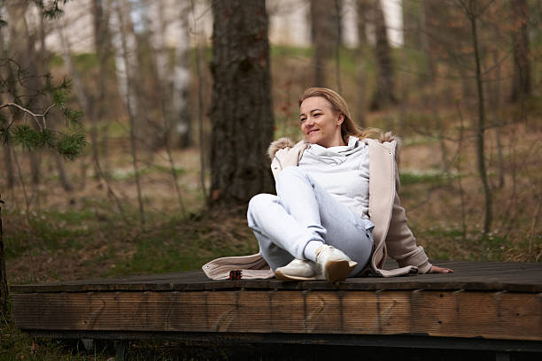 Woman sitting on a wooden boardwalk, smiling and looking away, surrounded by nature.