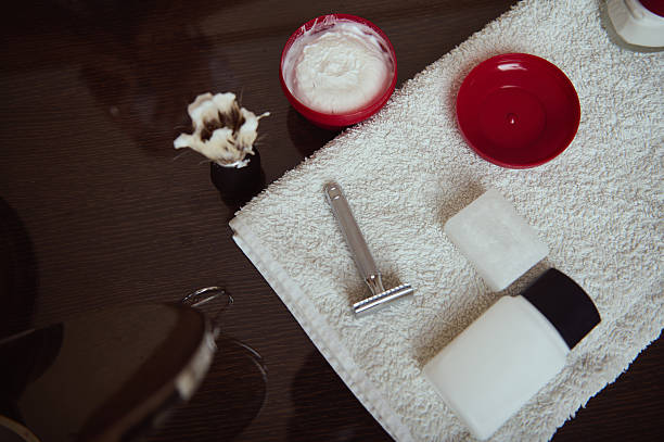 A tidy grooming scene featuring a razor, soap, a bar, cream, and a towel on a wooden vanity, conveying calm, clean, and traditional bathroom rituals.