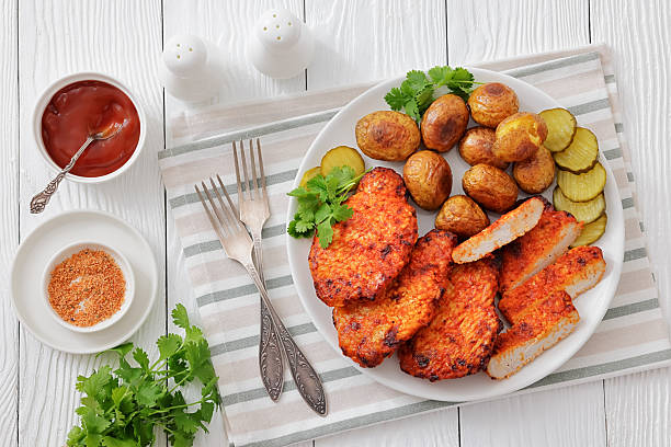 Paprika-Rubbed Pork Chops on a plate with cilantro, baked potatoes and sliced dill pickles on white wood table with forks and ketchup, flat lay, close-up, not AI generated