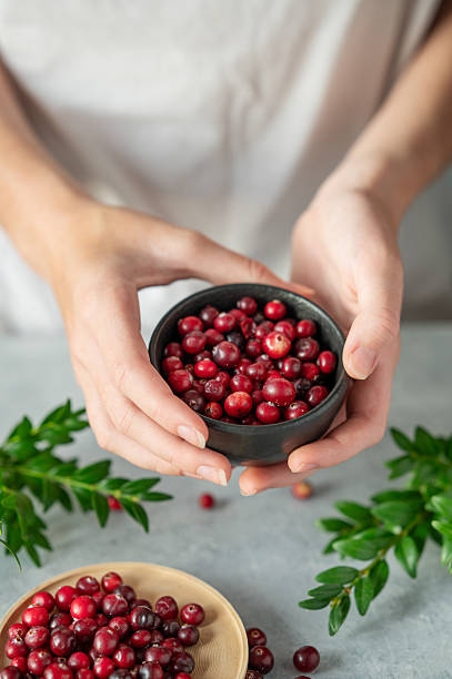 Hand holding bowl of fresh cranberries on a light table with green branch.