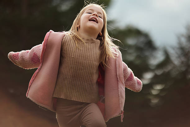 Little girl smiling, running with arms outspread, enjoying childhood in nature.