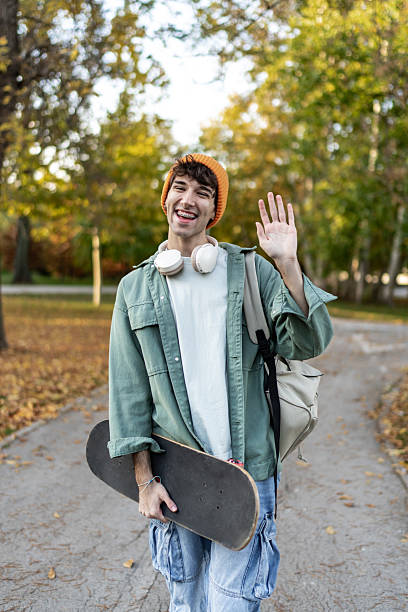 istock Happy young man walking in park waving hand 2244203331