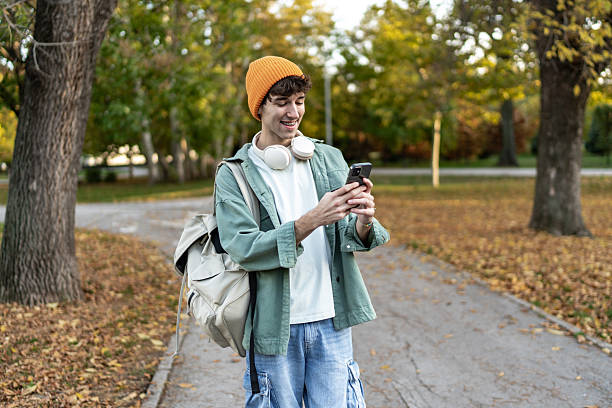 istock Young man smiling, browsing phone in autumn park 2244203379