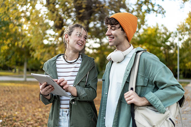 istock Young friends connecting outdoors, sharing digital tablet 2244203581