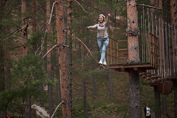 Young woman enjoying active leisure activity on high ropes obstacle course among pine trees.