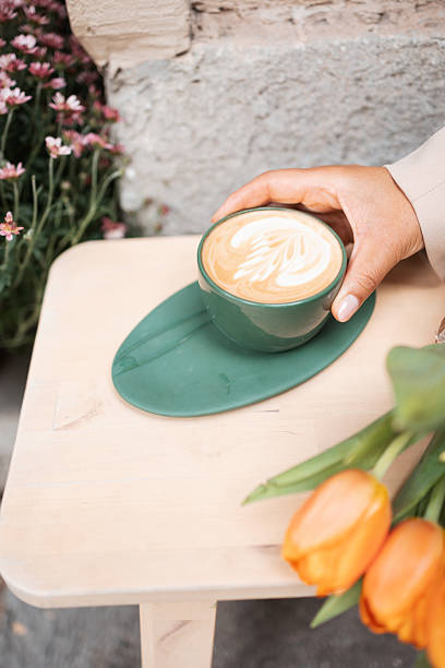 Hand holding cappuccino with latte art and fresh tulips