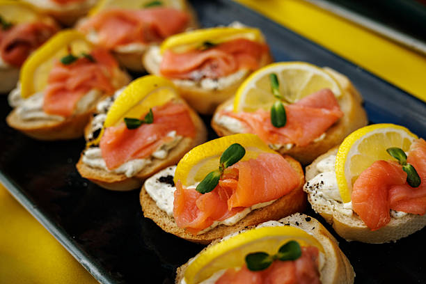 Close-up of canapes with smoked salmon, lemon slices, and cream cheese served on a dark tray.