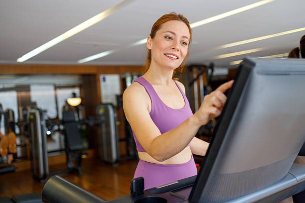 istock Smiling woman adjusts treadmill settings during a focused gym cardio workout in modern fitness club, wearing purple athletic wear 2244206697