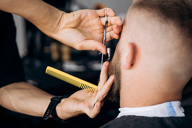 istock Barber cutting beard with scissors and comb for male client in barbershop. 2244207855