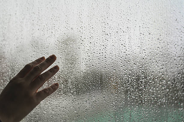istock Hand touching window with raindrops on a gloomy day 2244207879