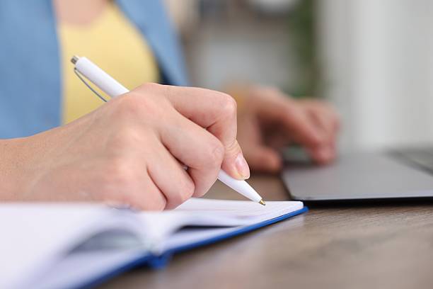 istock Woman taking notes while passing online test on laptop at wooden table indoors, closeup 2244209642