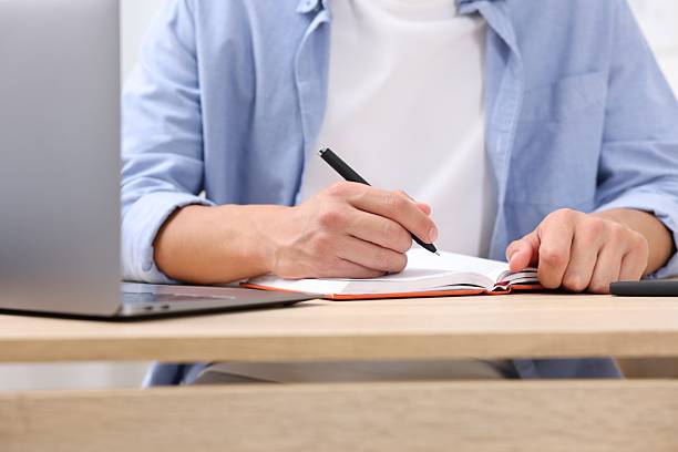 istock Man taking notes while passing online test via laptop at wooden table indoors, closeup 2244209673