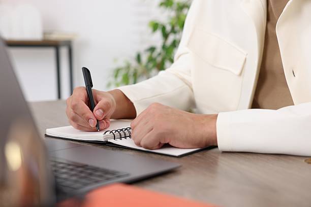 istock Man taking notes while passing online test via laptop at wooden table indoors, closeup 2244209687