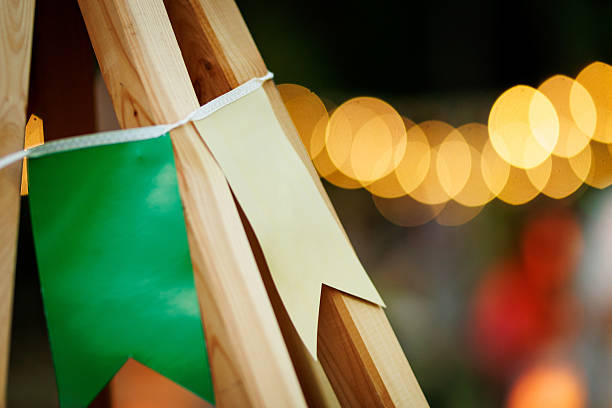 Close-up of green and yellow paper flags hanging on wooden frame with blurred festive lights in the background.
