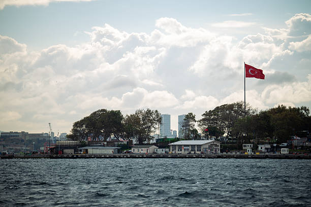 ISTANBUL, TURKEY – October 31, 2025: A large Turkish flag flies above low waterfront buildings along the Bosphorus on a breezy day under dramatic clouds.