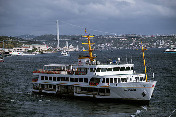 ISTANBUL, TURKEY – October 31, 2025: A municipal passenger ferry sails on the Bosphorus Strait on a windy day, with the Bosphorus Bridge (15 July Martyrs Bridge) and the city skyline visible in the background under dramatic clouds.