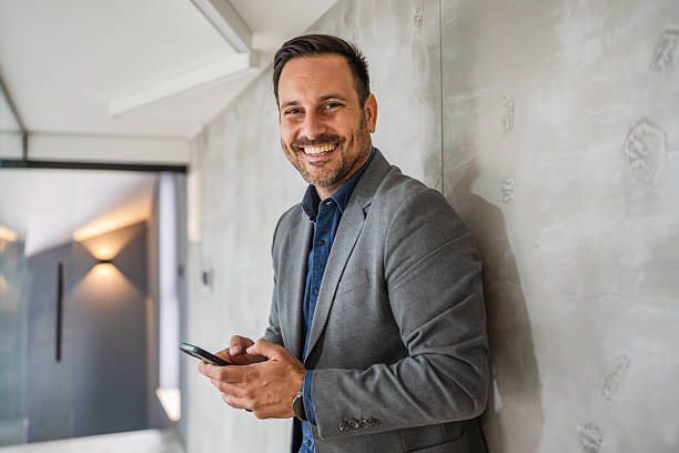 istock Smiling man holding phone connecting with technology in office 2244212660