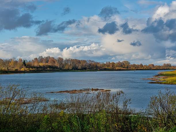 istock Tranquil autumn river scene with distant houses and a bright, cloudy sky 2244214907