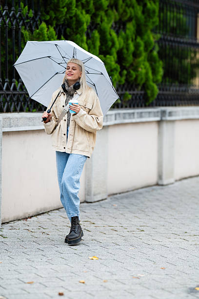 istock Young woman walking with umbrella and coffee cup 2244215659