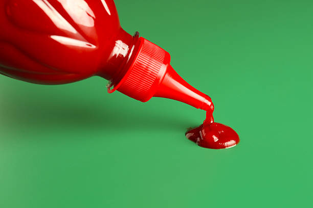 Squeezing ketchup from bottle on green background, closeup