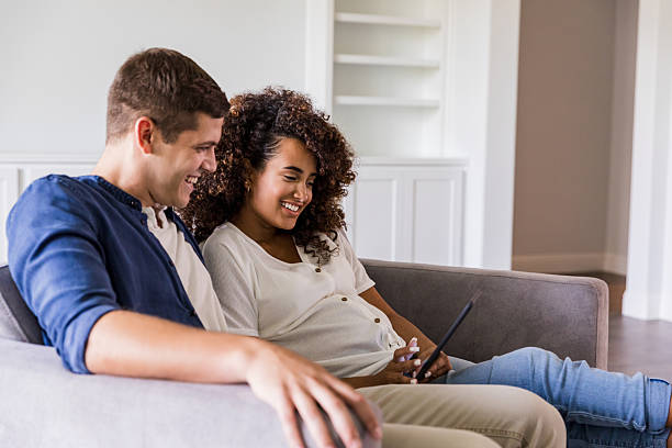 istock Happy couple laughing and looking at a digital tablet while relaxing on the couch 2244218221