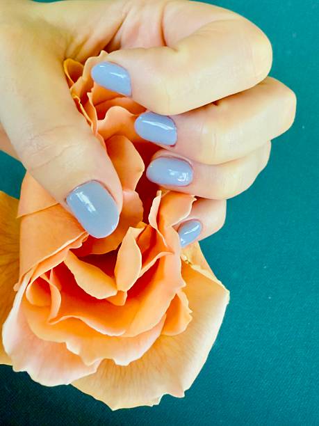 A close-up photograph of decorative nail art featuring colorful floral designs, a butterfly motif, and a pink heart accent applied over white nail polish. The fingers rest on a vibrant woven textile background, adding bright texture and contrast. This image highlights creative manicure styling, DIY nail decals, detailed hand care, and artistic beauty design.