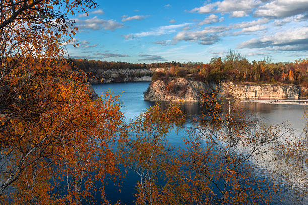 Orange and yellow foliage frames a calm lake nestled among limestone cliffs. The clear reflections and vivid colors capture the serenity and richness of autumn in nature.
