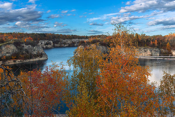Golden and red trees surround still blue water under soft afternoon light. The mix of color, texture, and mirror reflections highlights peaceful balance and natural beauty.