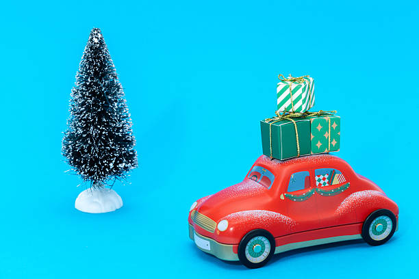 Christmas presents loaded onto the roof of a red car with a snowy Christmas tree
