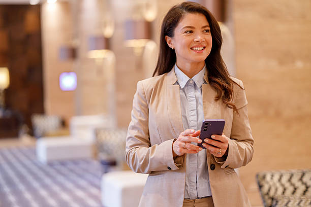 istock Professional businesswoman smiling while sending message on smartphone, staying connected in modern office lobby 2244230293