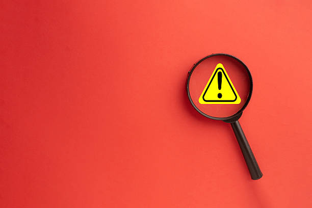 istock Focus on Risk: Magnifying Glass over Yellow Warning Alert Icon on Red Background 2244231922