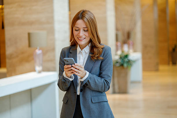 istock Businesswoman standing in a hotel lobby, smiling while using her mobile phone, messaging or browsing 2244233766