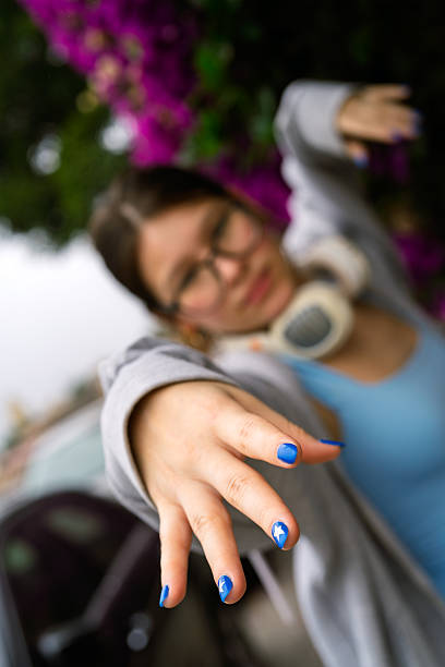 A soft focus image of a woman holding her hand up to block the sunlight in an outdoor garden. The bright sunlight filters through the green foliage of trees, and the woman’s hand is raised as a shield against the intense light.