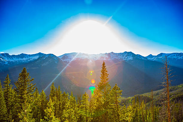 A radiant sunrise crowns the snow-capped Rocky Mountains, its light spilling across endless pine forests below. The image captures the intersection of heaven and earth — where brilliance meets tranquility. Sun flares cascade through the frame, painting the landscape with warm tones and creating a sense of ascension. The forest glows in golden-green hues while distant peaks stand in shadowed reverence beneath the expanding light. This composition evokes spiritual elevation, balance, and renewal — nature’s purest form of worship.