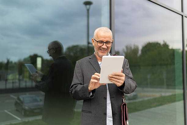istock Mature adult businessman smiling while using digital tablet outdoors 2244248190