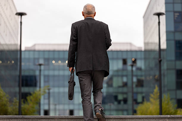 istock Senior businessman with briefcases walking towards office building 2244248318