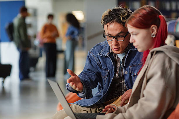 istock Young Asian Man Explaining Project to Young Caucasian Woman Using Laptop 2244252726