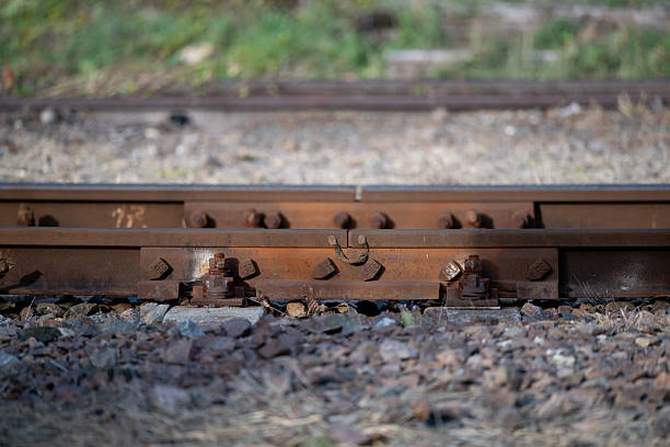A detailed view of a railway track joint where two metal rails are bolted together, showing signs of rust and weathering. The gravel bed and fasteners add to the industrial texture of the scene, capturing the raw mechanics of railway infrastructure up close.