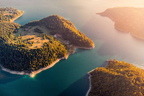 istock Aerial view discovering a tranquil lake surrounded by lush forests and small settlements under soft golden light 2244258845