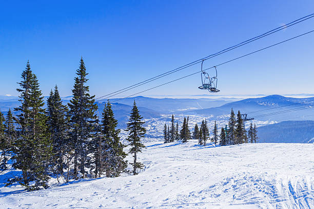istock Panoramic View from Green mount on Sheregesh ski resort, Altai mountains. Active winter rest, white snow ski slopes, tracks and chairlift, clear blue sky and forest. Atmosphere of mountain holiday. 2244262943