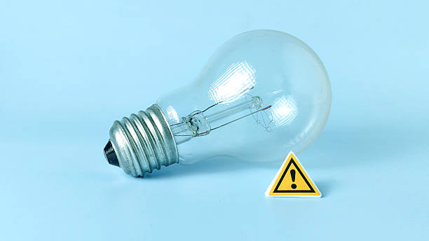 istock Incandescent Light Bulb Next to Caution Sign on Blue Background Representing Idea, Danger, and Energy 2244262972