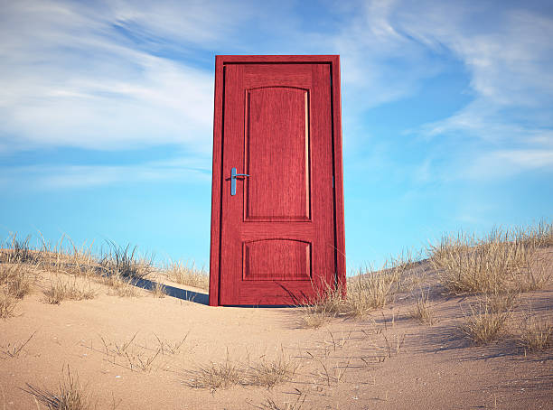 istock Colorful red door stands alone in a sandy landscape under a bright blue sky 2244263541