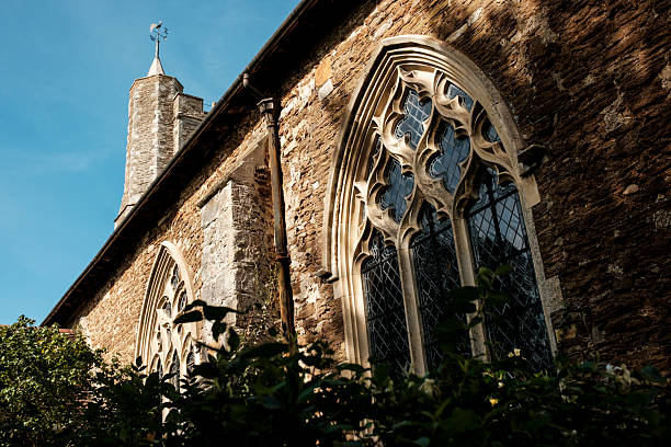 Stone facade of an ancient gothic church displaying intricate window tracery and a tall spire with a weather vane, capturing historic design elements under clear skies