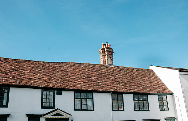 Old brick chimney rising from a classic tiled roof on a white traditional house, standing against a clear blue sky â charming, weathered architecture in a sunny village scene