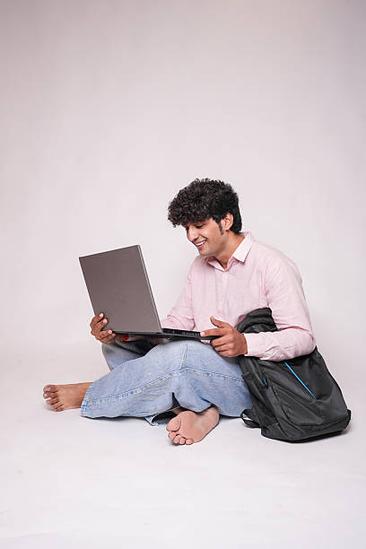 istock Young indian male college student e-learning on laptop while sitting isolated on white studio background. Asian Gen Z boy using computer. Education and knowledge. Copy space. 2244264007