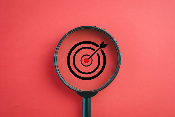 istock Focus on Objective: Magnifying glass over a target icon on red background. 2244265927