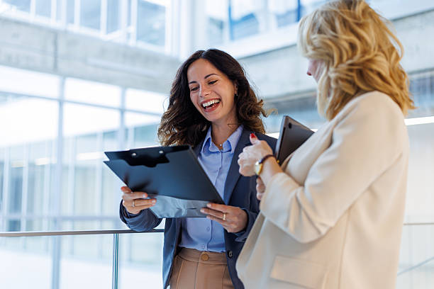 istock Businesswomen laughing while reviewing document on clipboard in office 2244267486