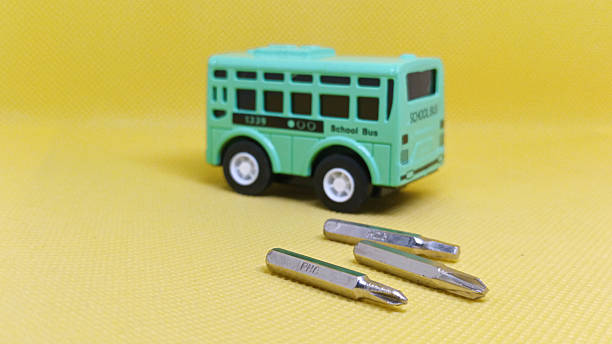 Miniature School Bus and Screwdriver Bits on a Yellow Background Symbolizing Repair, Maintenance, Education, and Childhood Themes