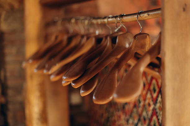 A collection of wooden hangers arranged on a clothes rail, photographed in a warm, rustic environment with a focus on textures and cozy ambiance, evoking organization, comfort, and contemporary simplicity.
