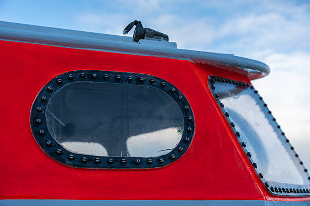 istock Bright red and gray metal boat cabin with oval windows and rivets under a blue sky. 2244272350